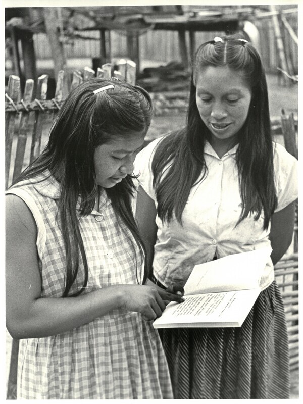 Photograph of Oncaye (left) and Dayuma (right) in Tewæno. Caption from V. Raymond Edman reads: "Oncaye from downriver Aucas being taught from Mark by Dayuma in Tewæno. Oncaye prays to return to her people, helped by Dywi and Tonia." While the photograph depicts Oncaye and Dayuma reviewing a print of the Gospel of Mark translated into Wao tededo, Dayuma had only limited literacy and communicated Bible stories or verses mostly from memory.