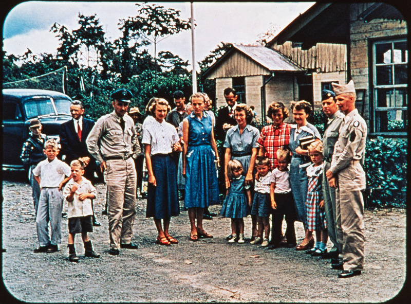Color image of Olive Fleming, Elisabeth Elliot, Barbara Youderian, Marilou McCully, and Marj Saint with some of the U.S. Army, Navy, and Air Force personnel who had helped with the search efforts, c. January 12-14, 1956. Frame from <i>Mid-Century Martyrs</i> filmstrip developed by HCJB, Mission Aviation Fellowship, and the five widows in 1956.