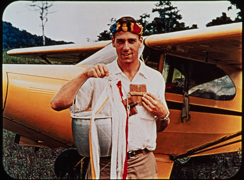 Photograph of Ed McCully in front of Nate Saint's Piper Cub with bucket used in the "bucket drops" over the Waorani settlement. Frame from <i>Mid-Century Martyrs</i> filmstrip developed by HCJB, Mission Aviation Fellowship, and the five widows in 1956.