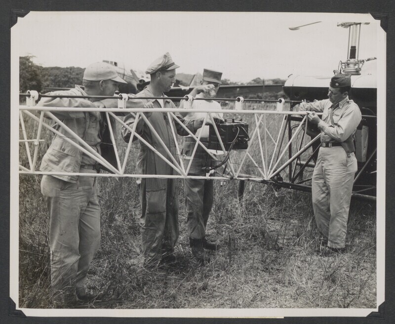 U.S. soldiers prepare helicopter for air search operations. The H-13 helicopter was piloted by Major Malcolm Nurnburg of the U.S. Air Force. The Air Force Rescue personnel were led by Major Nurnberg and Navy Captain Dewitt. Original USCARIB Central caption reads: "Making preparation for the first flight to the site of a massacre where five missionares are from left Navy Chief radioman, L. J. Moore of the Naval Mission to Ecuador, 1st Lt. James E. Claunch, 23rd Div Air Section; PFC Jerry J. Dick of 23rd Air Section and Major Malcolm Nurnberg US AF Mission to Ecuador. These were some of key personnel of the joint Army, Navy, Air Force search operation for five missionaries found murdered by the Auca Indians of Ecuador."