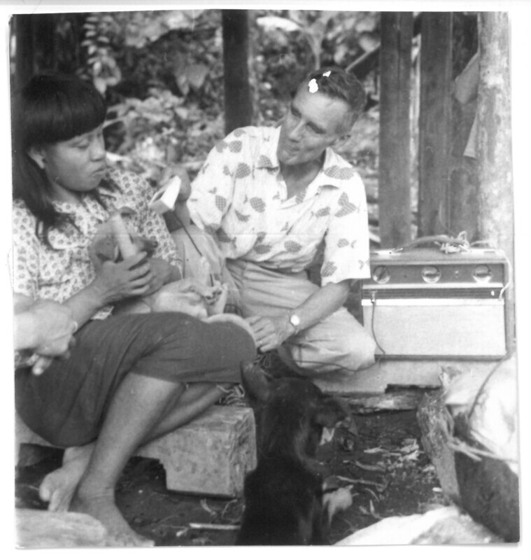 Photograph of Dr. Wilfred Tidmarsh holding dictaphone to record Waorani woman's speech, likely Mintaka (Mintaca) or Mankamo (Maengamo), c. 1957. Both Waorani women came out of the rainforest near Arajuno seeking news of their lost niece, Dayuma.